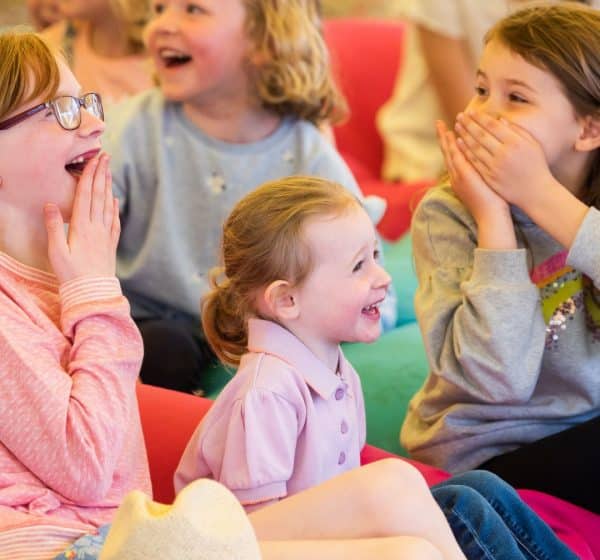 An audience of children laugh in surprise during storytelling.