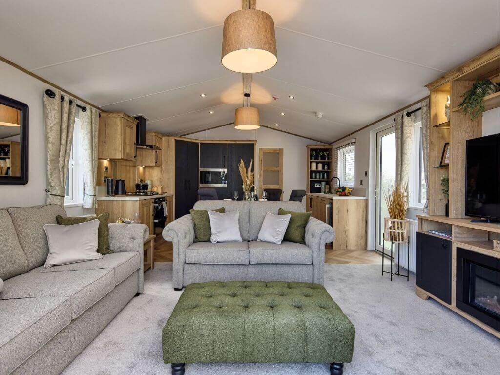 An interior shot of a modern, stylish caravan holiday home, showing the sofa and kitchen and dining spaces.