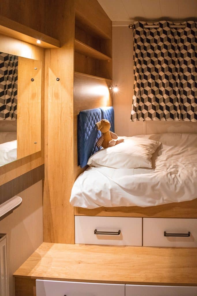 A teddy bear sits on the pillow of a single bed in a lodge at Pinewoods Holiday Park.