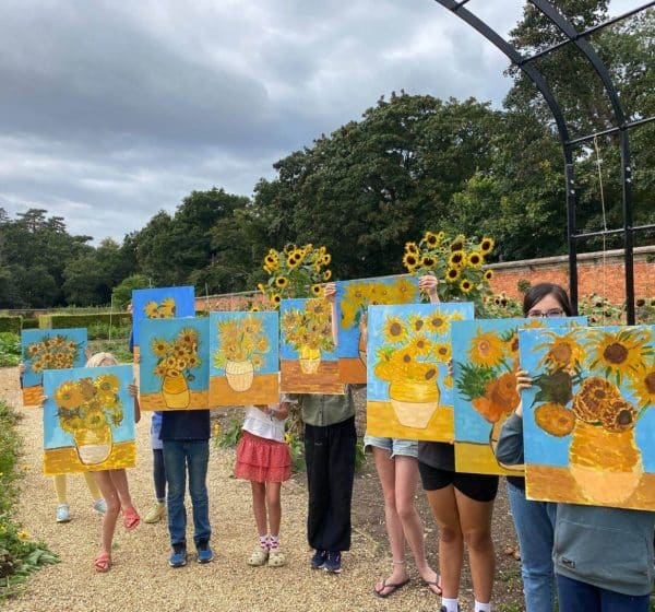 Children hold up their versions of Van Gogh's Sunflowers in Holkham Walled Garden, Norfolk