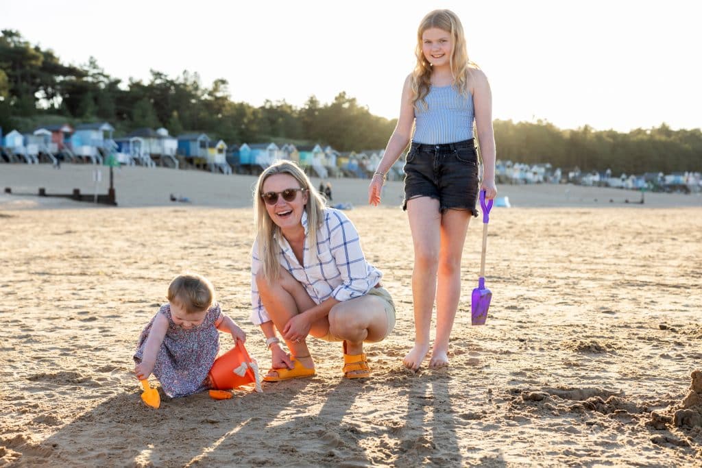 A mum, girl and toddler have fun on Wells Beach in the sunshine while on holiday in Norfolk