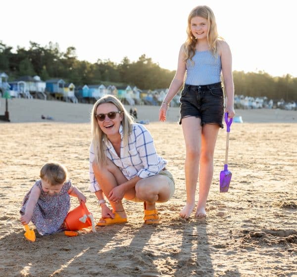 A mum, girl and toddler have fun on Wells Beach in the sunshine while on holiday in Norfolk