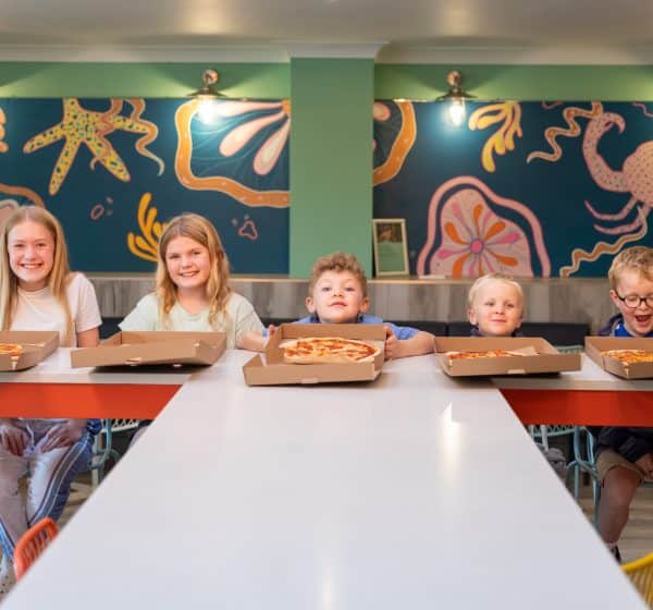 Five children sit inside a cafe, each with an open pizza box in front of them.