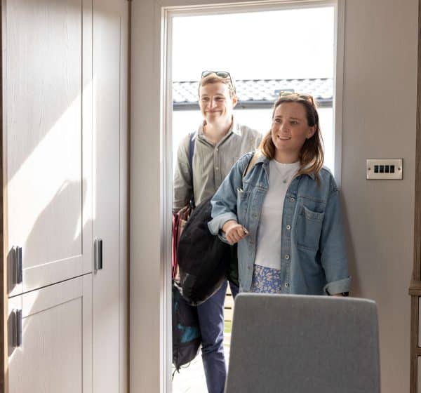 A couple walk through the door into a luxury holiday lodge, carrying bags and smiling