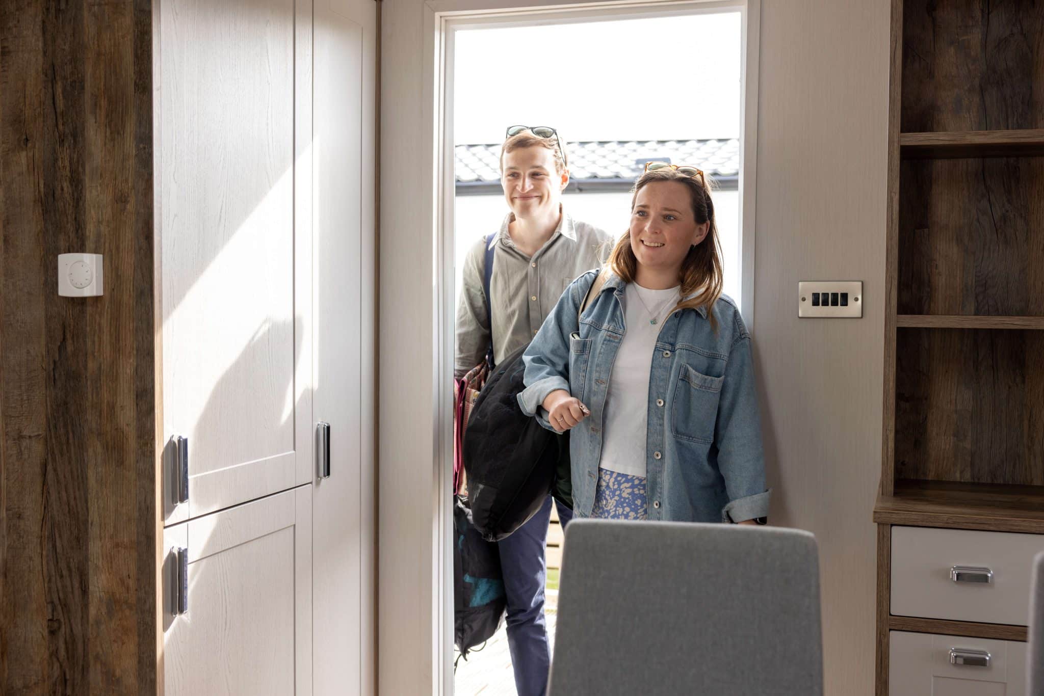 A couple walk through the door into a luxury holiday lodge, carrying bags and smiling