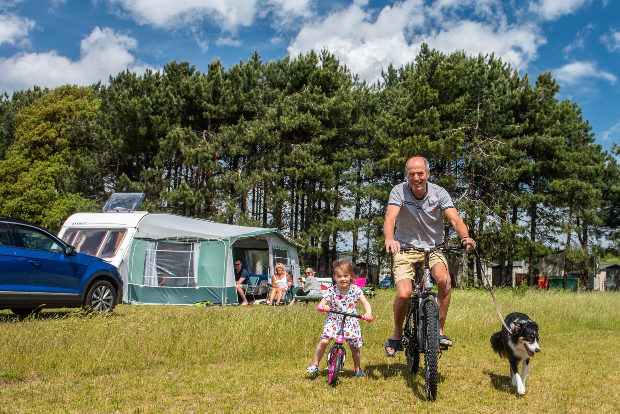 A man and little girl smile on their bikes, as more people look on from the awning of a caravan.