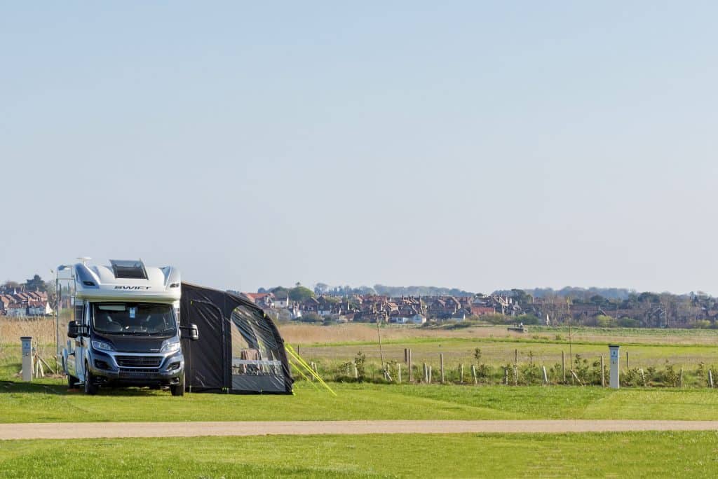 A motorhome and awning pitched on Pinewoods touring park, with views of Wells-next-the-Sea town in the background