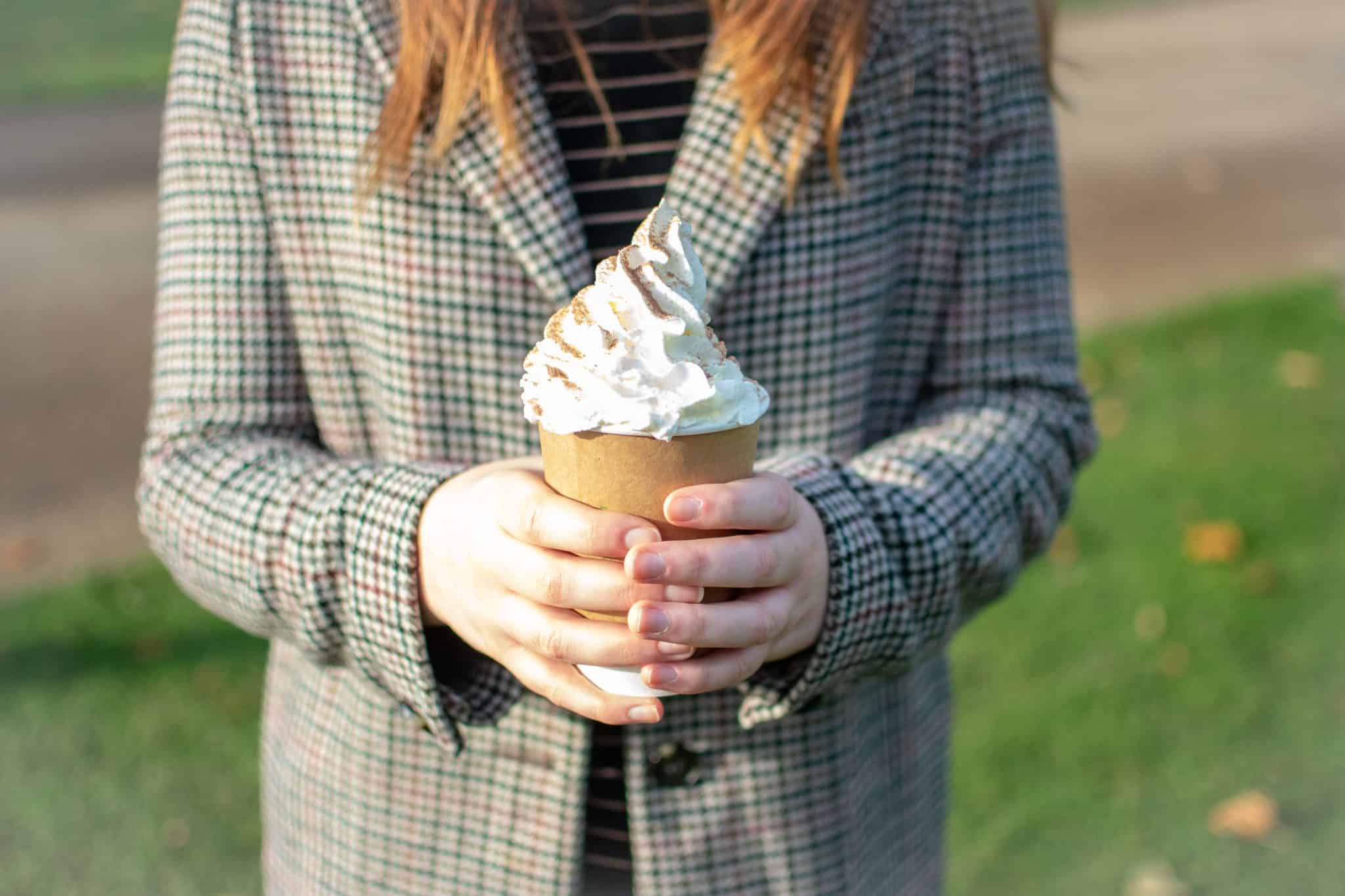 A woman holds a takeaway cup with a hot chocolate and cream