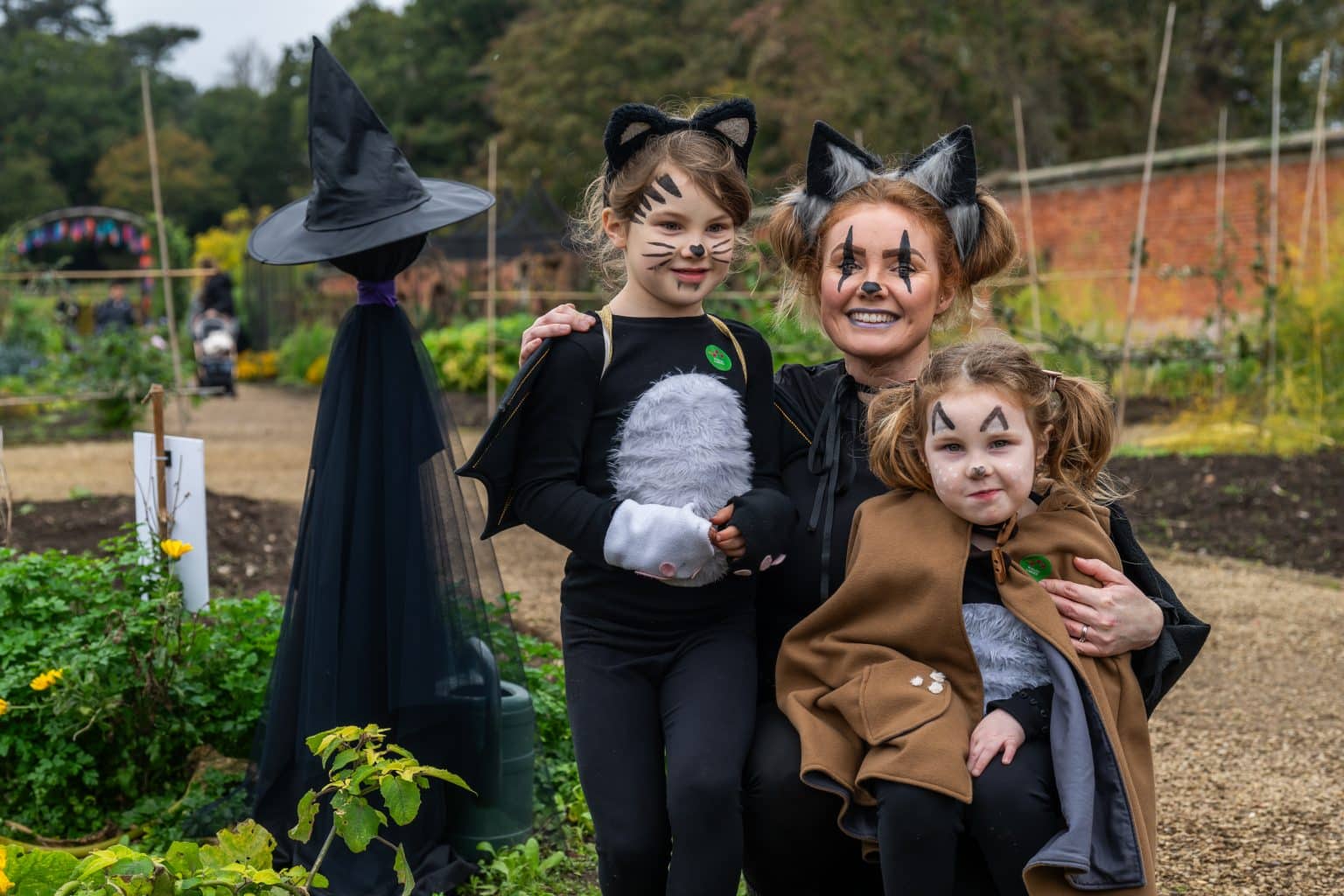 A family dressed up as cats for Halloween sit by a pretend witch in Holkham Walled Garden