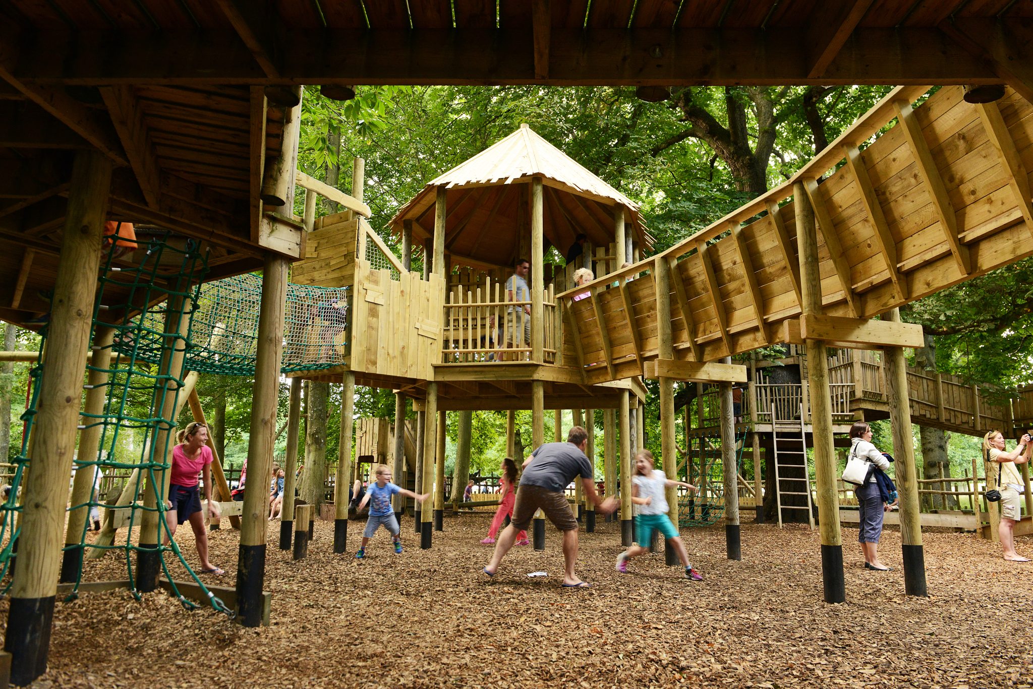 Children and some parents play in a play area in the trees