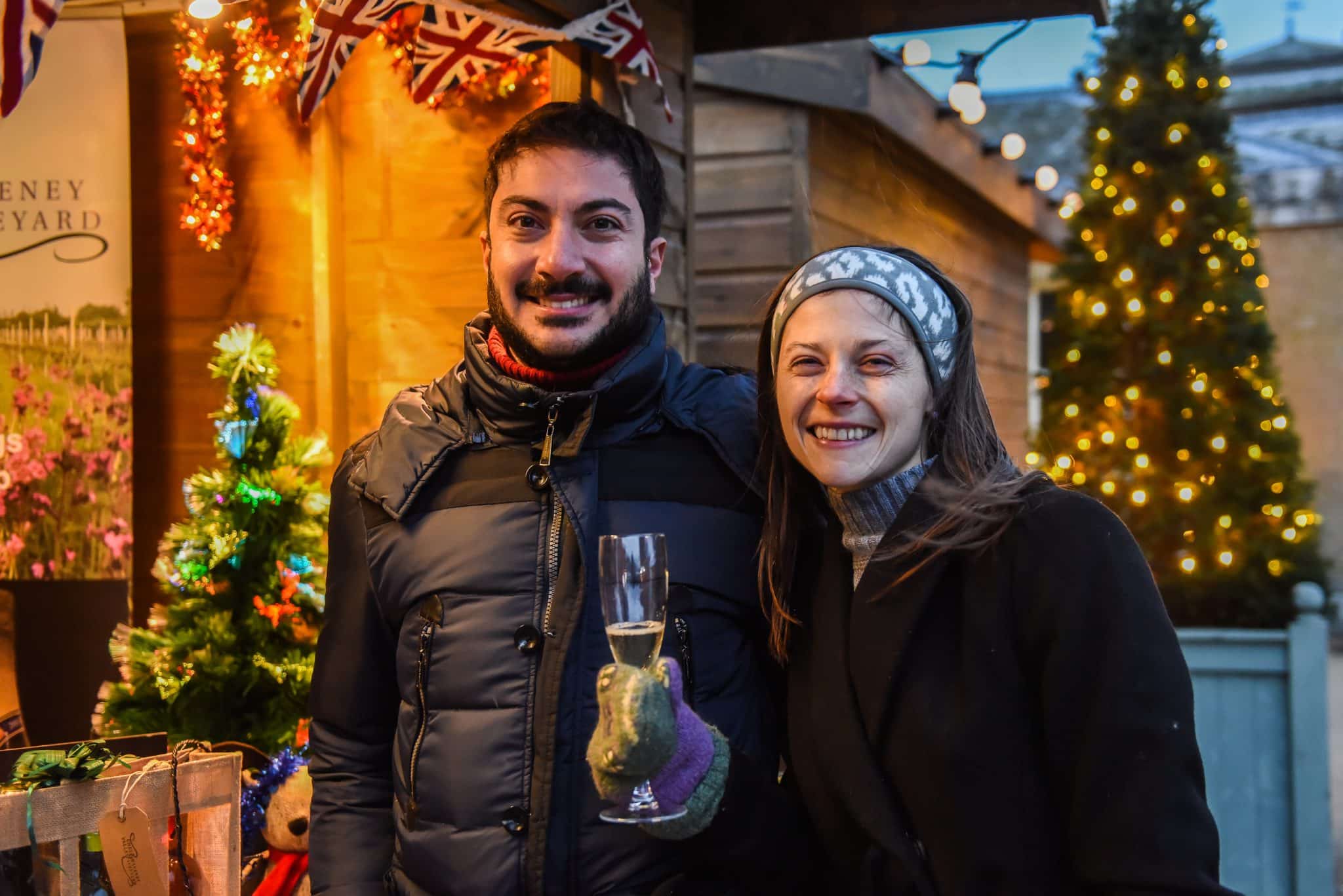 A couple at Holkham Christmas market with Christmas lights in the background